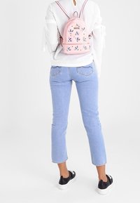 Růžový batoh s květinovou výšivkou, kulatý design, nastavitelné popruhy; spárován s světle modrými džínami a černými teniskami.