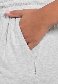 Grijze Baumwoll-Sweatpants mit strukturiertem Stoff, ausgestattet mit einer Seitentasche und einem elastischen Bund. Die Tasche hat ein kleines Reißverschlussdetail.