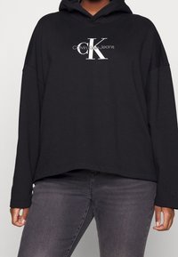 Felpa con cappuccio nera realizzata in morbido misto cotone, con il logo bianco di Calvin Klein Jeans sul petto e un design over-size.