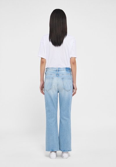 Jeans evazați de culoare albastru deschis, cu un finisaj decolorat, patru buzunare și cusături contrastante. Asortați cu un tricou alb simplu și pantofi albi.