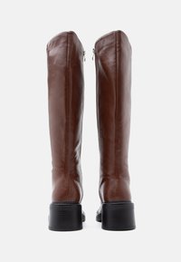 Καφέ δερμάτινες μπότες μέχρι το γόνατο με λείο φινίρισμα, στρογγυλεμένη μύτη, τακούνι μπλοκ και κλείσιμο με φερμουάρ στο πλάι.