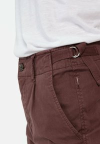 Burgundy cotton pants feature a button closure, side pockets, belt loops, and a fabric belt with a metal ring. Smooth, textured finish.
