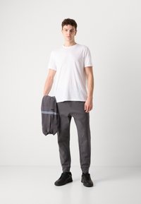 Tricou alb cu mânecă scurtă, pantaloni de trening gri conici și adidași negri. Ține un hanorac gri închis cu dungi albastre.