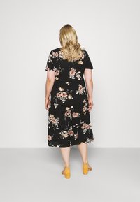 Mustakukkainen mekko lyhyillä hihoilla, jossa on kerroksellinen hame ja vaaleanpunaisia sekä valkoisia kukkakuosisia yksityiskohtia. Yhdistetty keltaisiin lohko-korko sandaaleihin.