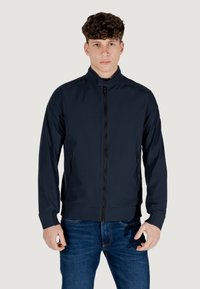 Giacca zip a collo alto di colore blu navy, con due tasche laterali e un design aderente. Realizzata in materiale liscio e leggero con polsini a coste.