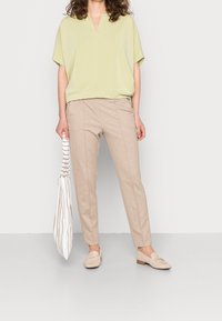 Ljusgrön kortärmad topp med V-ringning, parat med beiga smala byxor. Håller en randig tygväska och bär ljusa loafers.