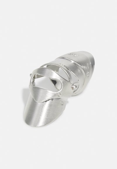 Silbernes, metallisches Schuhstück mit glatter, geschwungener Form, verstellbaren Riemen und einer visierartigen Vorderseite. Besitzt eine gebürstete Textur und subtile Hardware-Details.