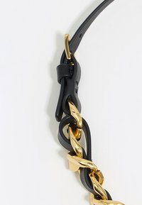 Schwarzes Lederband mit verflochtenen goldenen Metallkettenakzenten. Hat eine glatte Textur und einen geschlungenen Verschluss für eine verstellbare Länge.