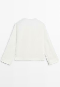 Chemise blanche unie à manches longues et col rond, étalée à plat montrant le dos, fabriquée en tissu lisse avec un ourlet droit.