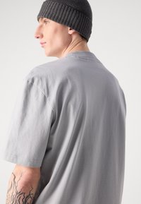 Graues Baumwoll-T-Shirt mit kurzen Ärmeln, rundem Ausschnitt, glatter Textur und lässiger Passform. Getragen mit einer gerippten grauen Mütze.