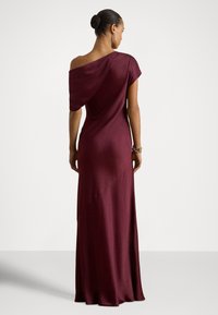 Vestido longo cor vinho em tecido suave e drapeado; apresenta um design de um ombro só e costuras assimétricas. Destaca-se pelo brilho sutil e pela silhueta ajustada.