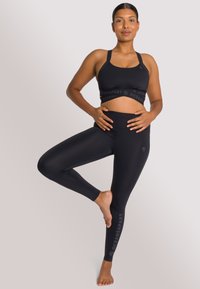 Zwarte sportbeha met logoband en high-waisted leggings, beide gemaakt van rekbaar materiaal, met een aansluitend ontwerp en een stijlvolle afwerking.