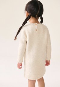 Robe en tricot couleur crème avec une texture duveteuse, épaules tombantes et ourlet arrondi. Dotée de trois boutons dans le dos.