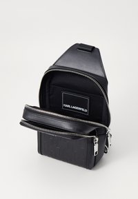 Black backpack with a textured fabric and smooth leather accents. Features a zipper closure and a logo tag inside. Compact and structured design.