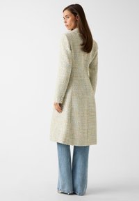 Licht gestructureerde, pastelkleurige wollen jas met een getailleerde pasvorm, lange mouwen en knopen aan de manchetten, gecombineerd met uitlopende blauwe spijkerbroeken.