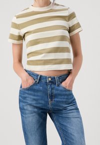 Offertopp i olivgrön och vit randig, korta ärmar, i bomull. Matchad med blå högmidjade jeans med knapp och fickor.