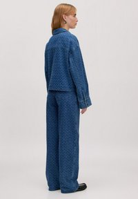 Blaue Jeansjacke und Hose Set mit einem strukturierten Muster. Die Jacke hat einen Kragen und eine leicht übergroße Passform, mit Knopfmanschetten.