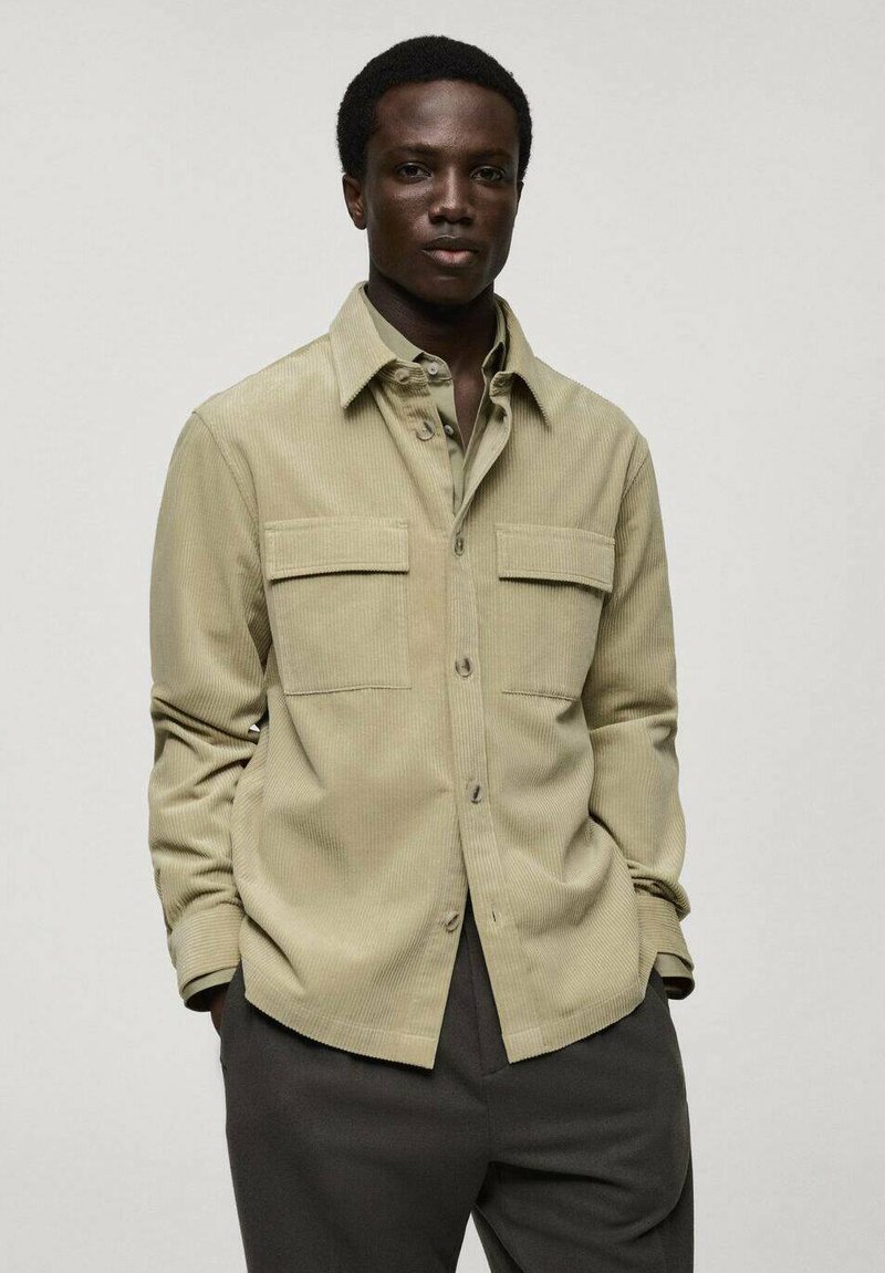 Groene corduroy shirt met een gespreide kraag, twee borstzakken en knopen aan de voorkant, gecombineerd met donkere broek. Glad materiaal en een relaxte pasvorm.