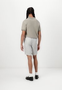 Grå polo-skjorte og lysegrå rutete shorts, vist fra bak. antrekket har korte ermer og er kombinert med svarte sko.