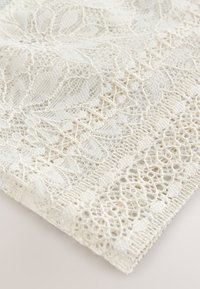 Tessuto in pizzo bianco con motivi floreali e geometrici, che mostra un lavoro a giorno intricato e cuciture strutturate.
