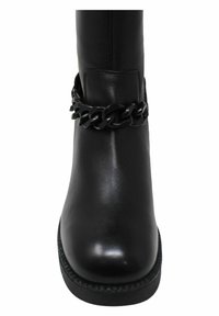 Stivale alla caviglia in pelle nera con un accento di catena nera corposa, texture liscia, punta rotonda e suola nera spessa con bordo decorato.