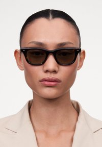 Occhiali da sole tartarugati con lenti marroni, caratterizzati da una montatura spessa e audace e un sottile logo sui tempietti. Finitura liscia e lucida.