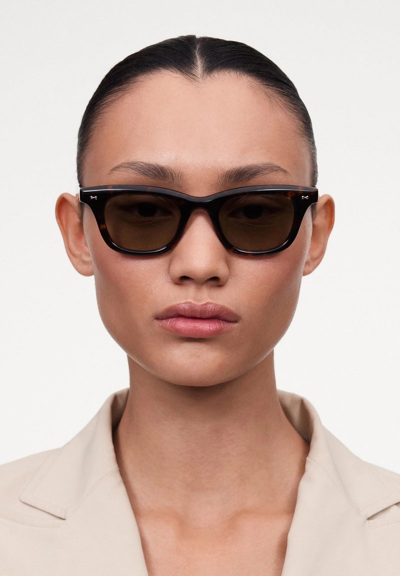 Occhiali da sole tartarugati con lenti marroni, caratterizzati da una montatura spessa e audace e un sottile logo sui tempietti. Finitura liscia e lucida.