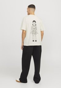 Camiseta color crema con una ilustración gráfica negra de una chica con un vestido en la parte posterior. Diseño holgado, mangas cortas, material de algodón.