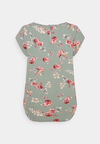 Blumenbluse aus hellgrünem Stoff mit roten und rosa Rosen. Verfügt über einen runden Ausschnitt und kurze Ärmel, mit einem Reißverschlussdetail auf der Rückseite.