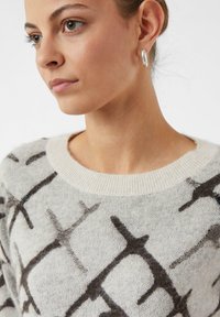 Sweter dzianinowy w jasnym beżu z ciemnobrązowym geometrycznym wzorem. Posiada ribbrowany okrągły dekolt i miękką teksturę. Prosty design z minimalnymi zdobieniami.