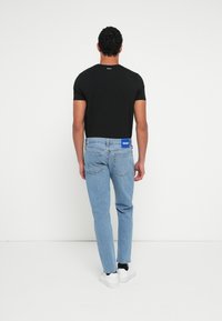 Czarny t-shirt z krótkim rękawem i jasnoniebieskie dżinsy z niebieską metką z tyłu. Dżinsy mają prosty krój i widoczne detale przeszyć.