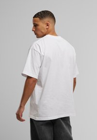 T-shirt en coton blanc avec une coupe décontractée, col rond et manches courtes. Présente une texture lisse et un design simple.