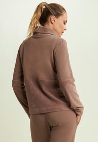 Pullover in pile marrone con colletto alto e texture contrastante in basso. Maniche lunghe, tessuto liscio e vestibilità morbida.
