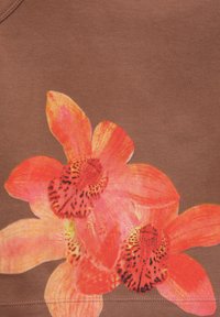 Design di fiori di orchidea arancioni e rosa vivaci stampato su uno sfondo di tessuto marrone con cuciture visibili vicino al bordo inferiore.