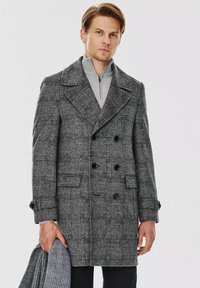 Dwurzędowy płaszcz w czarno-białą kratkę, wykonany z teksturowanej tkaniny, z dużymi klapami, przednimi kieszeniami i akcentami guzika.