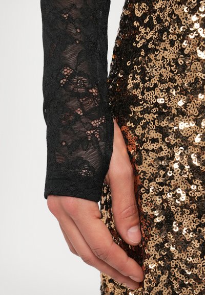 Un haut en dentelle noire à manches longues avec des motifs floraux délicats, associé à un vêtement à sequins avec des sequins circulaires dorés et cuivrés.