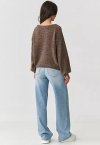 Brązowy sweter z dzianiny o luźnym kroju, szerokimi rękawami i żebrowanym wykończeniem, w połączeniu z jasnoniebieskimi jeansami z wysokim stanem i białymi trampkami.