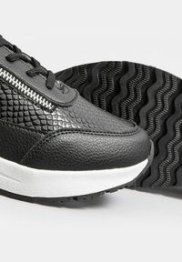 Black sneakers featuring textured leather and snake-like pattern, with white midsole and rubber outsole displaying a wavy tread design.