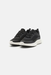 Schwarze Sportschuhe aus Netz- und synthetischem Material mit einem strukturierten Design, weißer Gummisohle und schwarzen Schnürsenkeln.