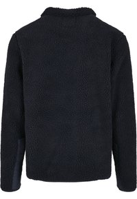 Veste en polaire noire à surface texturée, manches longues et col montant, vue de dos sur un fond blanc.