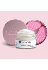 Crème contour des yeux Miracle au Thé Blanc de Teaology dans un pot en verre rond, texture de crème blanche, étiquetée avec les détails du produit, à côté d'une boîte en métal rose.