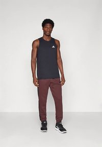 Svart ermeløs trenings-tanktopp med hvit logo, kombinert med burgunderrøde, innsnevrede bukser med sidestriper, og svarte joggesko.