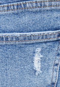 Tela de mezclilla azul claro con un parche deshilachado, costuras en naranja que contrastan a lo largo de las costuras y una textura suave.