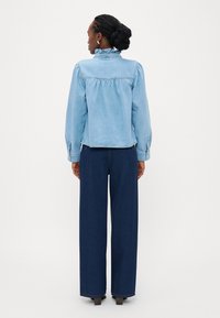 Ανοιχτό μπλε τζιν μπουφάν με βολάν στον γιακά και μακριά φουσκωτά μανίκια. Σκούρο μπλε παντελόνι με φαρδιά γραμμή. Λείος υφασμάτινος τύπος, άνετη εφαρμογή.