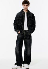 Donkerdenim jacket met borstzakken, gecombineerd met bijpassende baggy donkere jeans. G gedragen over een wit T-shirt; aangevuld met witte sneakers.