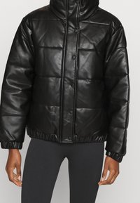 Doudoune noire en simili cuir avec un col haut, des boutons pression et un ourlet et des poignets élastiqués ; présente un design matelassé rembourré.