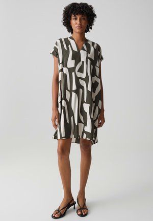 Donna con capelli ricci che indossa un vestito largo a maniche corte, lunghezza al ginocchio, con motivo astratto bianco e nero e tacchi neri con cinturini.