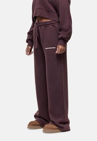 Losse, donkerbordeaux sweatpants van zachte stof met een elastische tailleband en logodetail, gecombineerd met bruine instappers.