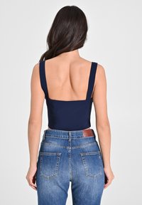 Top senza maniche di colore blu navy con un design a schiena quadrata, abbinato a jeans in denim azzurri a vita alta con tasche posteriori e una cintura marrone.