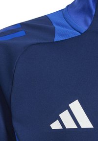 Marineblauwe sportshirt van textuurstof, met blauwe accenten op de schouder en een opvallend wit logo met drie diagonale strepen.